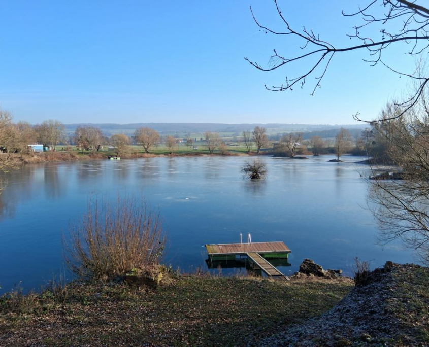 Wintersonne am zugefrorenen See Zugefrorener See im Winter bei blauem Himmel – Blick über das Eis mit Steg am Ufer