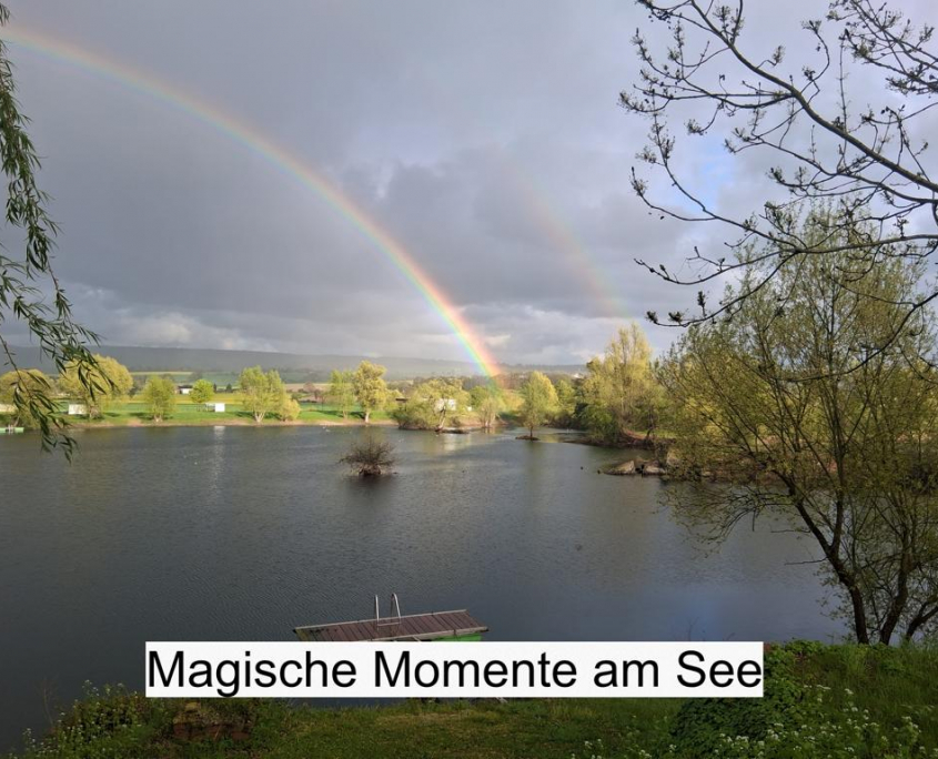 Seeansicht mit Steg, Bäumen und doppeltem Regenbogen